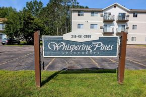 Cloquet apartment for rent - A sign for Whispering Pines Apartments stands in front of a building.