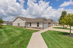 Dayton apartment for rent - A house with a brown roof and a grey garage door is surrounded by a grassy lawn and a sidewalk.