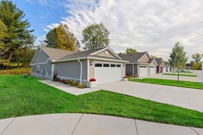 Lansing apartment for rent - A house with a grey garage door is surrounded by a green lawn.