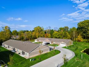 Lansing apartment for rent - A large building with a grey roof is surrounded by green grass and trees.