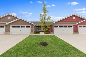 Groveport apartment for rent - A tree is planted in the middle of a grassy area in front of a two-story house with garages.