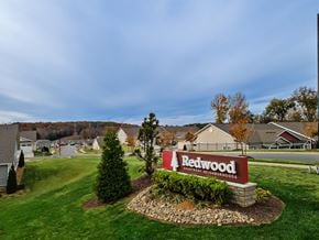 Kannapolis apartment for rent - A sign for Redwood Apartment Neighborhoods is in the foreground of a grassy area.