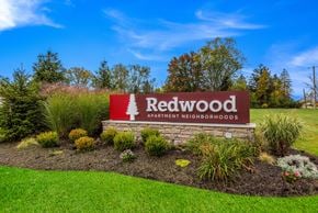 Macomb apartment for rent - A sign for Redwood Apartment Neighborhoods is surrounded by plants and grass.