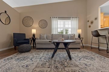 Perrysburg apartment for rent - A living room with a grey sofa, a black armchair, a round ottoman, a table with a lamp and a rug.