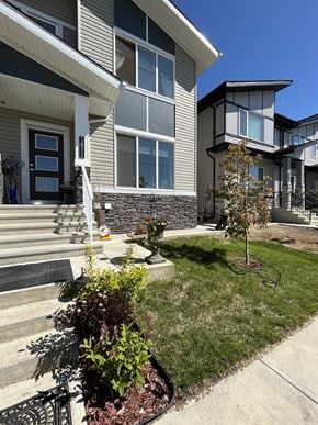 Edmonton apartment for rent - A house with a grey siding and a black door is surrounded by a well-kept lawn and a small tree.