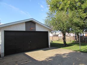 Edmonton apartment for rent - A garage with a black door and a tree in front.