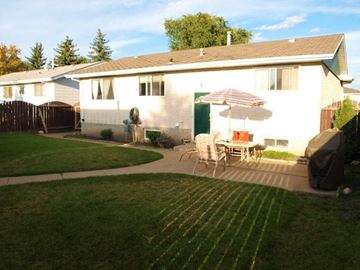 Edmonton apartment for rent - A house with a white exterior and a brown roof with a patio and lawn in front.