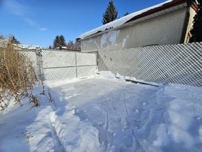 Edmonton apartment for rent - A snow-covered yard with a fence and a house in the background.