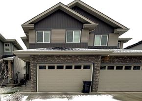Leduc triplex for rent - A house with a grey garage door and a brick pillar.