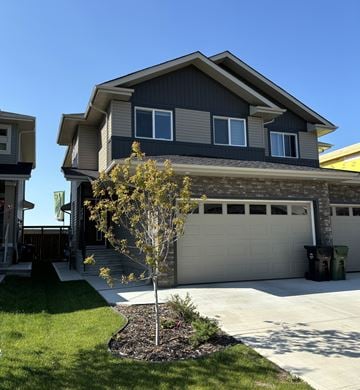 Leduc triplex for rent - A house with a grey garage door and a tree in front.