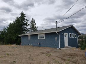 West Kelowna house for rent - A blue house with a white door and windows sits in a field.