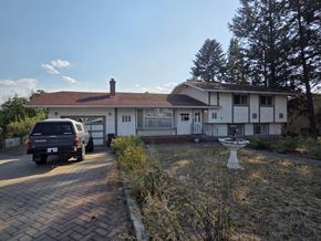 Kelowna apartment for rent - A house with a white exterior and a brown roof is shown with a car parked in front.