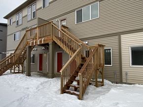 Leduc triplex for rent - A wooden staircase in front of a house with snow on the ground.