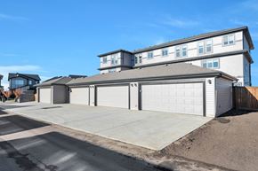 Leduc triplex for rent - A large house with a grey roof and white garage doors.