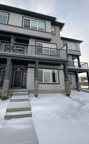 Leduc triplex for rent - A snow-covered walkway leads to a two-story building with a balcony.