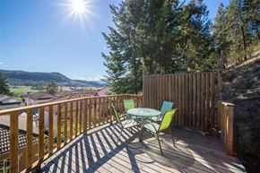 Kelowna apartment for rent - A wooden deck with a table and chairs overlooking a valley.