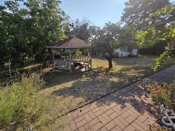 Kelowna apartment for rent - A gazebo is surrounded by trees and bushes in a backyard.
