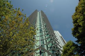 Vancouver condo for rent - A tall building with a green glass facade stands between two trees.