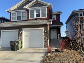 Leduc triplex for rent - A two-story house with a red and brown exterior and a white garage door.