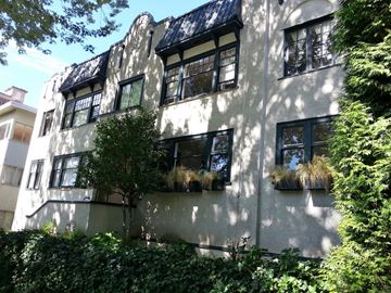 Vancouver apartment for rent - A white building with black windows and balconies is surrounded by greenery.