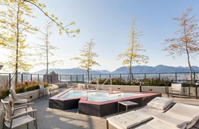 Vancouver condo for rent - A hot tub is surrounded by chairs on a patio with trees and mountains in the background.