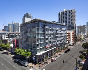 San Diego apartment for rent - A modern building with glass windows is in the foreground of a city street.