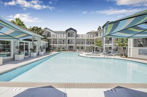 Pleasanton apartment for rent - A large swimming pool is surrounded by a white fence and a white building.