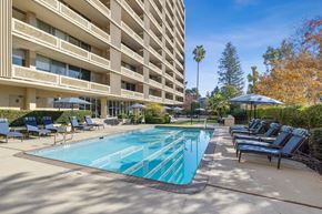 Palo Alto apartment for rent - A large swimming pool surrounded by lounge chairs and umbrellas in front of a multi-story apartment building.