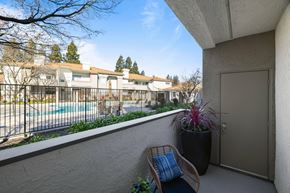 Livermore apartment for rent - A balcony with a chair and a potted plant overlooks a pool and apartment buildings.