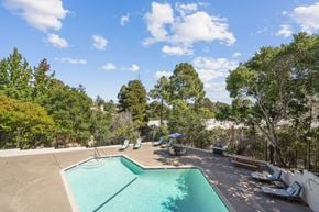 Belmont apartment for rent - a swimming pool with chairs around it and trees in the background