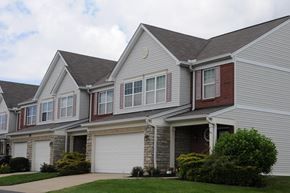 Richwood apartment for rent - A grey house with a red brick chimney and a white garage door at The Legends at Steeplechase Apartments, Richwood
