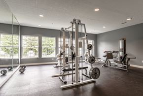 Mason apartment for rent - A spacious gym with a variety of equipment including a squat rack, bench press, and dumbbells at Twin Fountains Apartments, Mason, OH