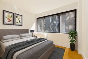 New York apartment for rent - A bedroom with a bed, two pictures on the wall, a potted plant, and a window with a view of a building outside.