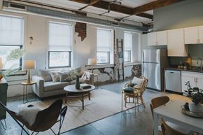 St. Louis apartment for rent - A modern living room with a white couch, a wooden chair, and a kitchen area with a refrigerator.