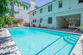 Sherman Oaks apartment for rent - a swimming pool in front of a white building with chairs on the side
