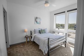 Richfield apartment for rent - A bedroom with a bed, a nightstand with a lamp, and a window overlooking a parking lot.