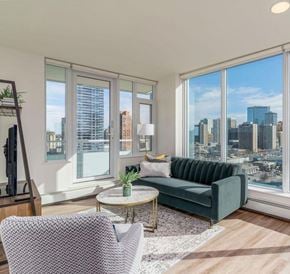 Calgary apartment for rent - A living room with a green couch and a large window overlooking a cityscape.