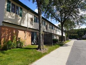 Taylor townhouse for rent - A tree stands in front of a building with a red brick wall.