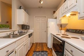 Chattanooga apartment for rent - A kitchen with white cabinets and appliances, a sink, and a door in the background.