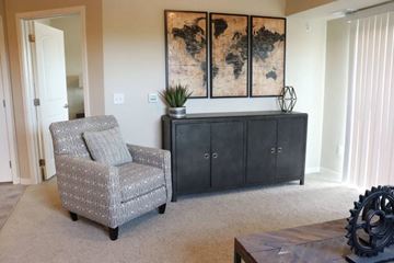 Otsego apartment for rent - A grey armchair sits in a living room with a black cabinet and a painting on the wall.