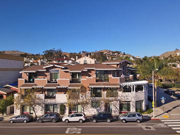 Ventura condo for rent - A building with a white facade and a brown roof with a parking lot in front of it.