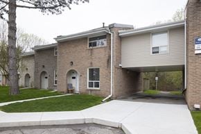 Oshawa apartment for rent - Brick buildings with white doors and a sidewalk in front.