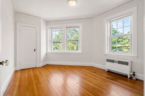 Cambridge apartment for rent - A room with wooden floors and white walls has a window with a view of trees.