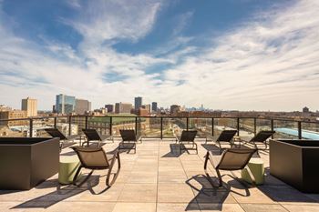 An outdoor terrace with lounge chairs and tables with a view of the city