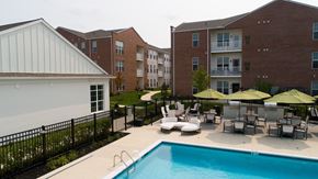Mechanicsburg apartment for rent - A pool surrounded by chairs and umbrellas in front of apartment buildings.