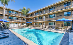 Riverside apartment for rent - A swimming pool in front of a building with lounge chairs and umbrellas.