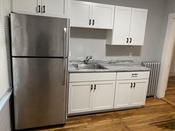 Jamaica Plain apartment for rent - A kitchen with a stainless steel refrigerator and white cabinets.
