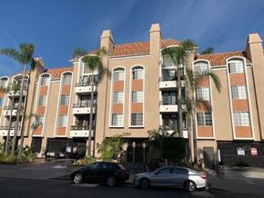 Los Angeles apartment for rent - A large apartment building with a black car and a silver car parked in front.