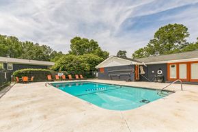 Spartanburg apartment for rent - A large outdoor swimming pool surrounded by orange chairs and trees.