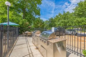 Prattville apartment for rent - A barbecue grill is situated on a patio with a metal fence and trees in the background.